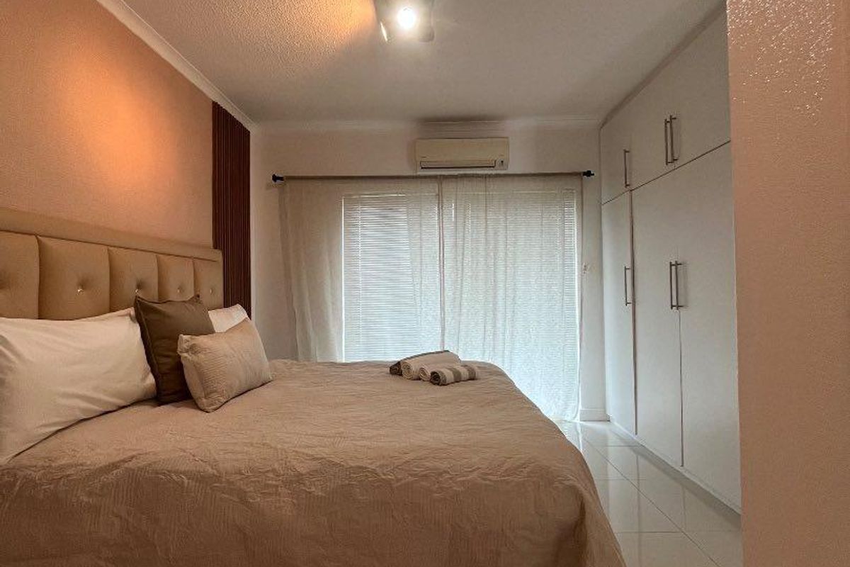 A well-maintained bedroom featuring built-in cupboards, tiled flooring, and an integrated air conditioning unit, with access to a balcony through sliding doors.