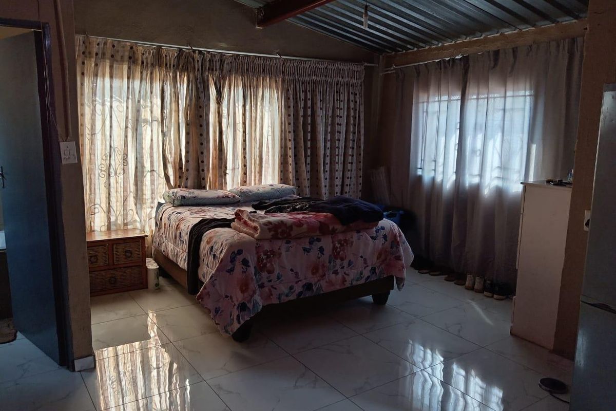 A bedroom featuring polished marble-look floor tiles, large windows with curtains, and an exposed industrial-style corrugated metal ceiling.