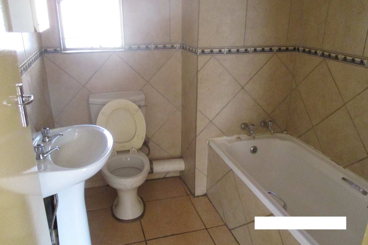 A dated bathroom featuring a pedestal basin, toilet, and bathtub with full-height wall tiling and floor tiles.