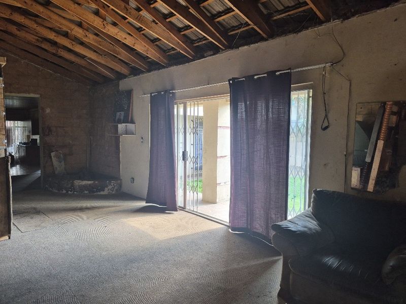 Spacious living area featuring exposed timber roof trusses, sliding glass doors with security gates, and significant potential for renovation and interior finishing.