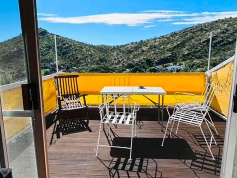 A sunny balcony featuring timber decking, a retractable yellow awning, and expansive mountain views, accessible through a large sliding glass door.