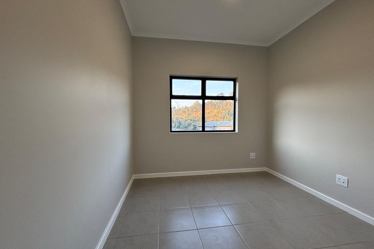 A clean, empty bedroom featuring neutral wall tones, tiled flooring, and a black-framed window providing natural light and exterior views.