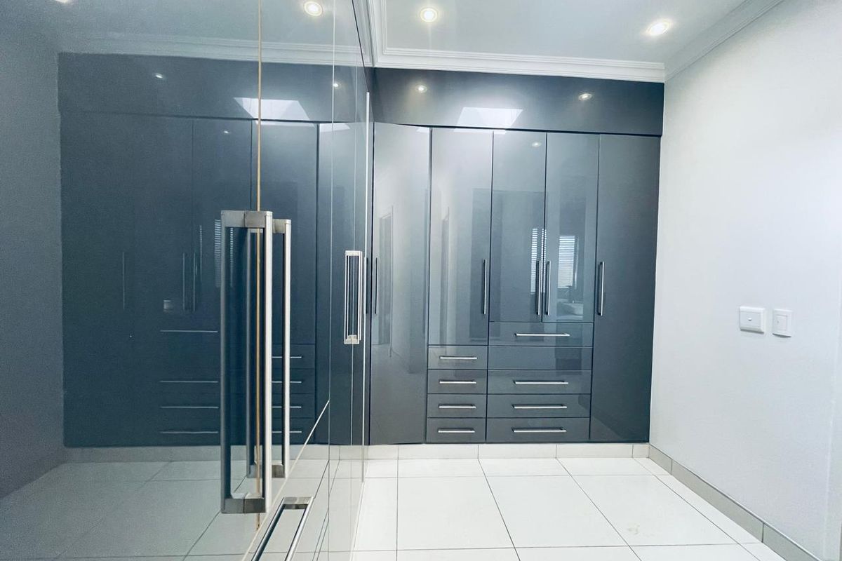 Modern bedroom featuring high-gloss grey built-in cupboards with mirrored sliding doors, sleek tiled flooring, and recessed downlighting.