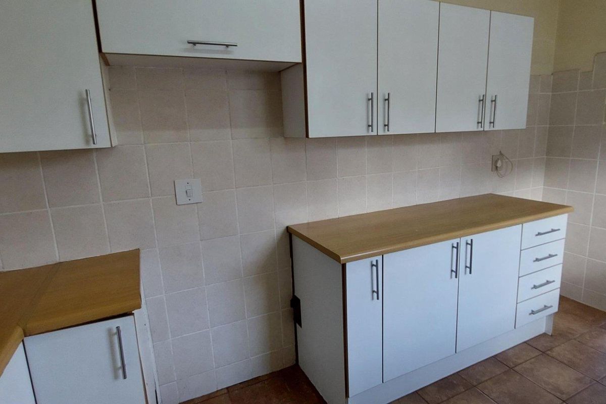 A functional kitchen area featuring white cabinetry, light wood-look countertops, and tiled splashbacks with tiled flooring.