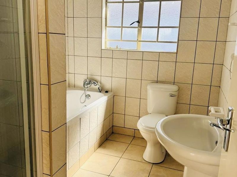 A functional bathroom featuring a pedestal basin, toilet, built-in bathtub, and a separate shower enclosure with neutral wall and floor tiling.