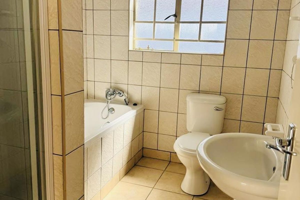 A functional bathroom featuring a pedestal basin, toilet, built-in bathtub, and a separate shower enclosure with neutral wall and floor tiling.
