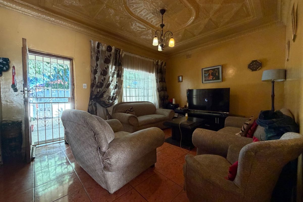 A living room featuring traditional pressed metal ceilings and tiled flooring, with direct access to the exterior through a security gate.