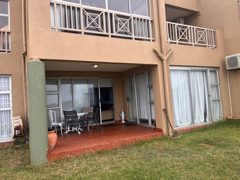 Ground floor patio area with tiled flooring and sliding glass doors, featuring an upper-level balcony and exterior building facade.