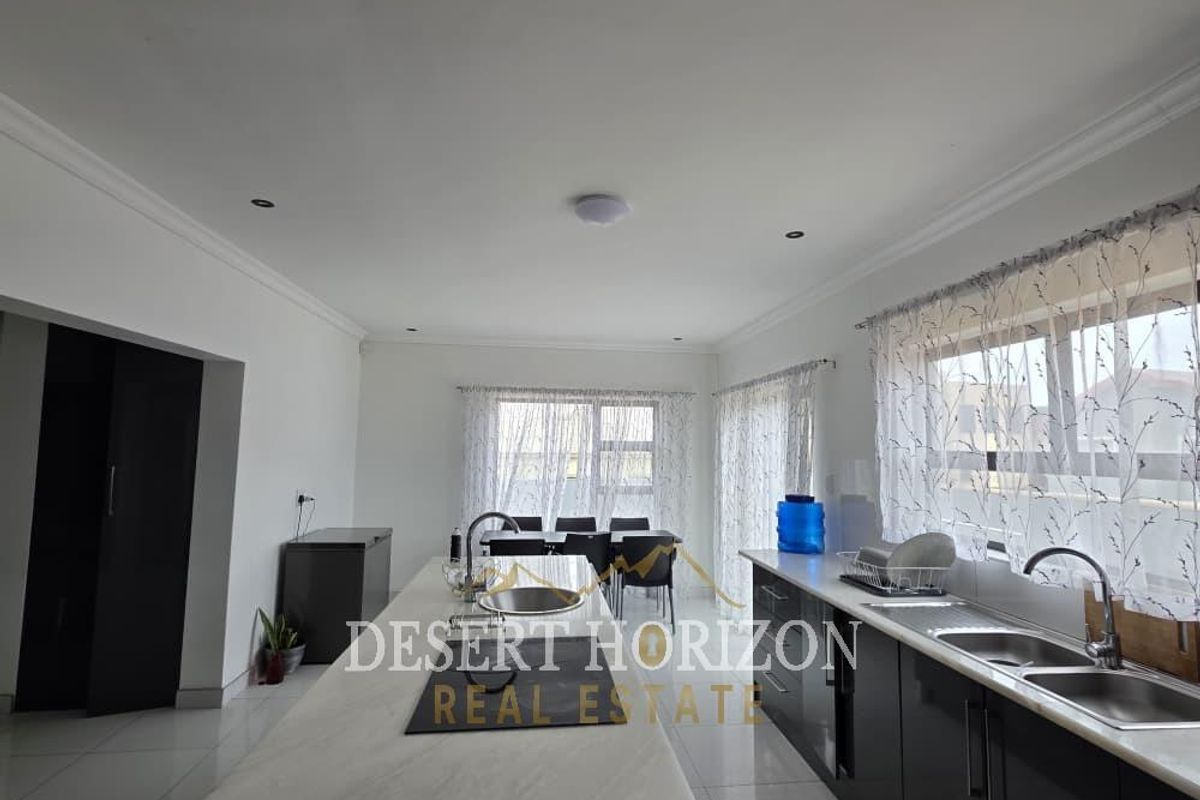 Modern kitchen featuring a large central island with stone countertops, double sink, and sleek dark cabinetry, offering a bright and functional workspace.
