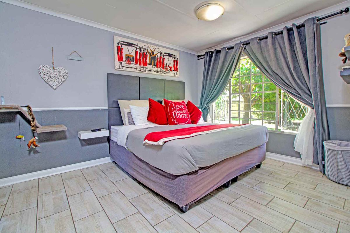 A bedroom featuring tiled flooring, a large window with curtains, and a built-in headboard panel.