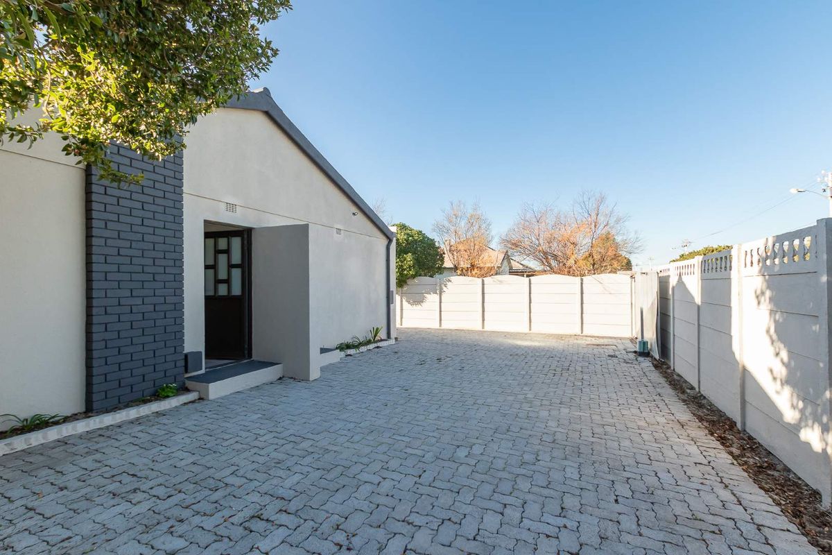 Rear exterior view featuring a paved driveway, secure precast concrete boundary walls, and a modern brick-accented building facade.