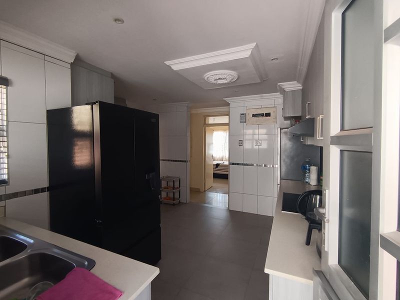 A functional kitchen featuring built-in cabinetry, stone countertops, a double bowl sink, and a tiled splashback, with a view leading into the adjacent living area.