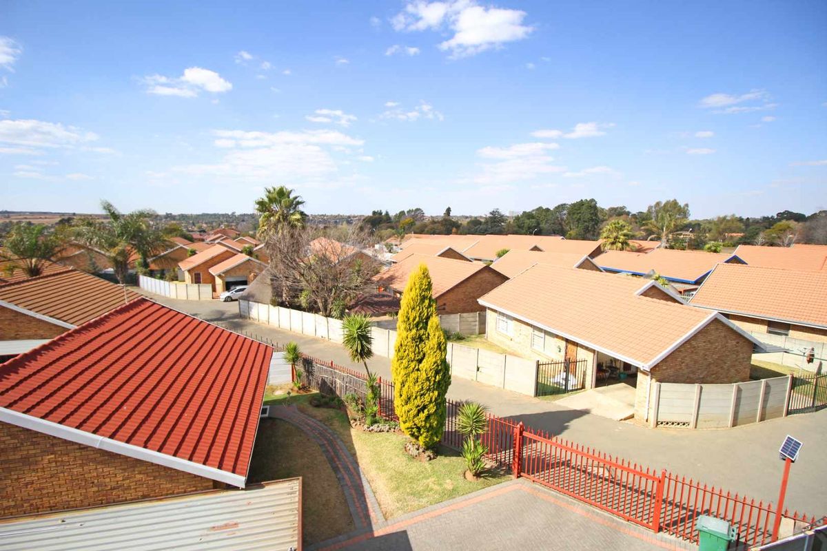 An elevated aerial view of a residential complex featuring brick houses with tiled roofs, paved driveways, and perimeter fencing.