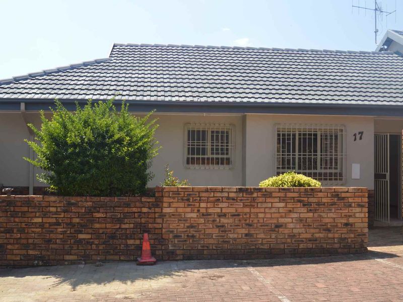 Front elevation of a townhouse featuring a tiled roof, brick boundary wall, and paved driveway access.