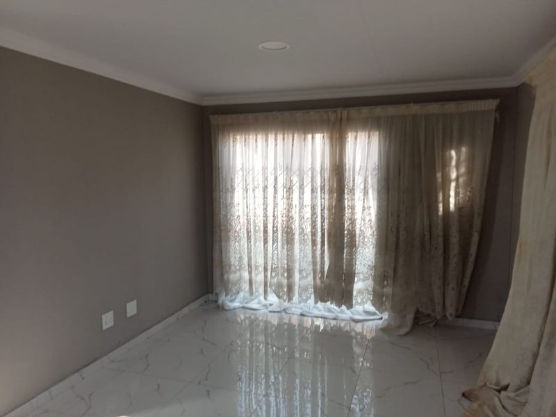 A bright, empty living room featuring polished marble-look floor tiles, recessed downlighting, and large sliding glass doors with elegant sheer curtains.