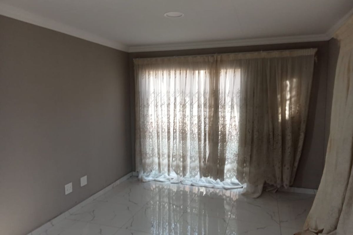 A bright, empty living room featuring polished marble-look floor tiles, recessed downlighting, and large sliding glass doors with elegant sheer curtains.