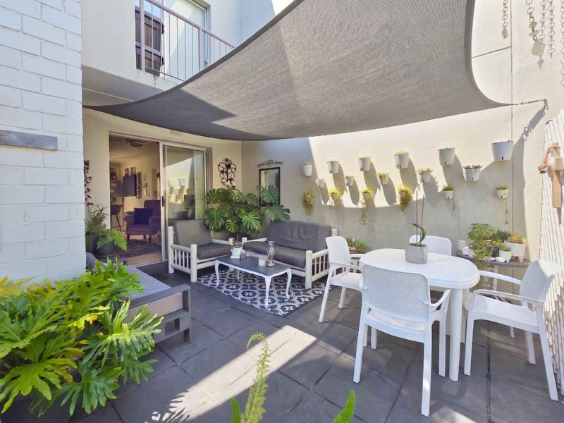 A well-maintained outdoor patio area featuring tiled flooring, a shade sail, and direct access to the interior through a sliding glass door.