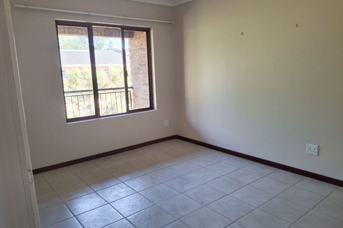 A vacant bedroom featuring neutral tiled flooring, a large window with exterior views, and standard electrical outlets.