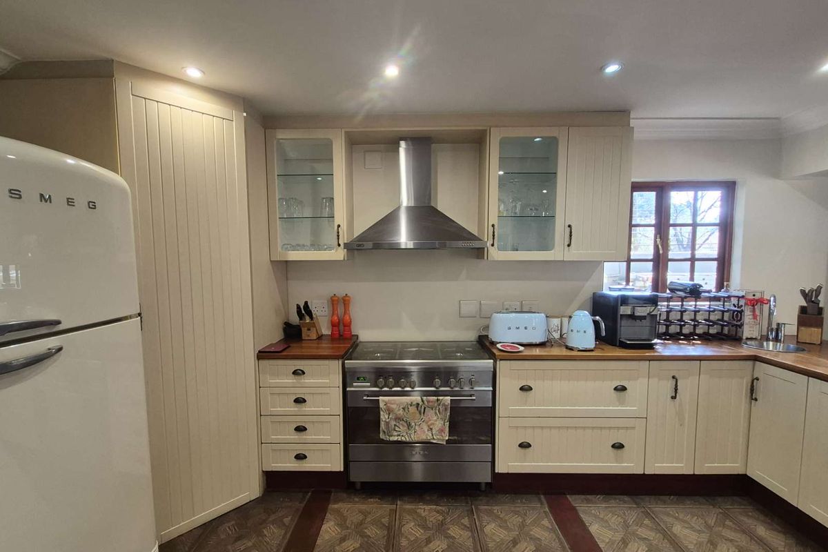 A well-maintained kitchen featuring cream-colored cabinetry, wooden countertops, a stainless steel oven with extractor fan, and recessed ceiling lighting.