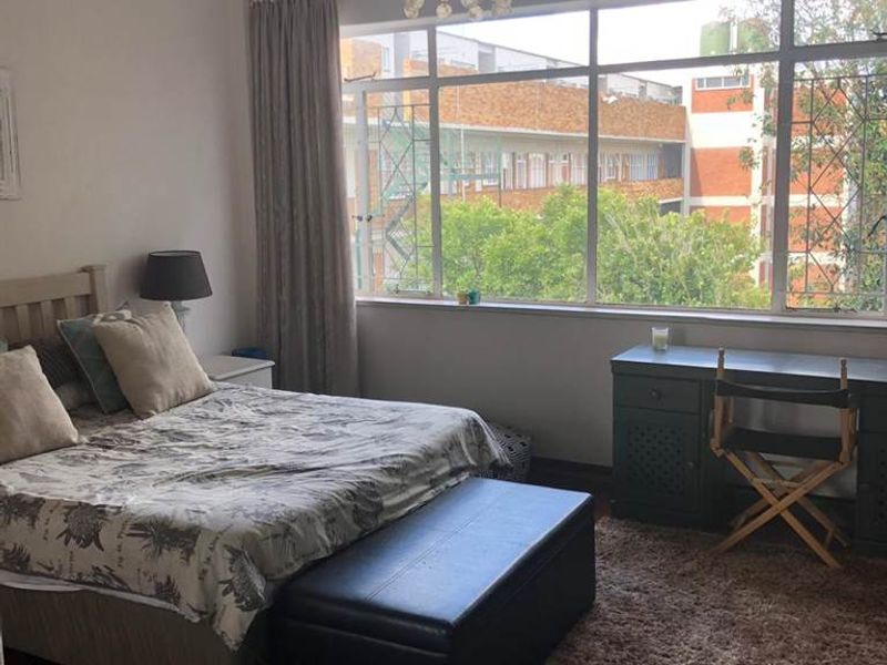 A spacious bedroom featuring large windows that provide natural light, parquet flooring, and classic cornicing details.