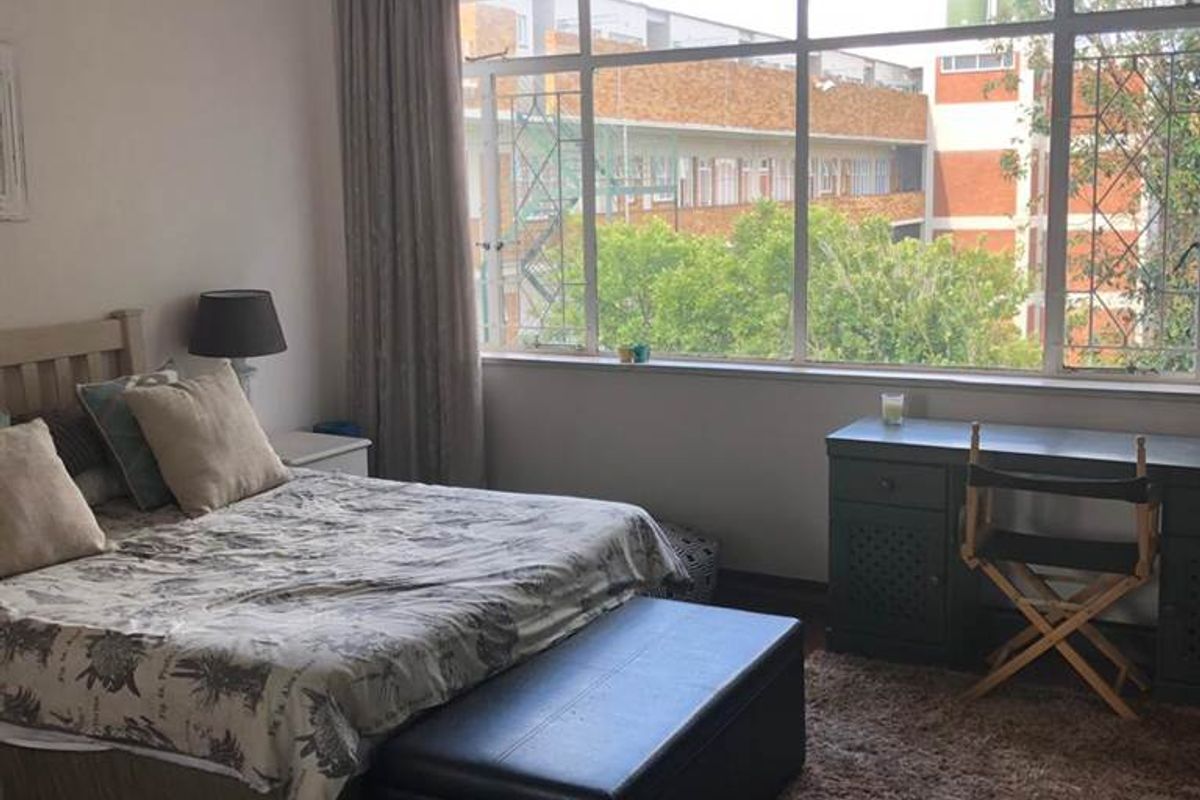 A spacious bedroom featuring large windows that provide natural light, parquet flooring, and classic cornicing details.
