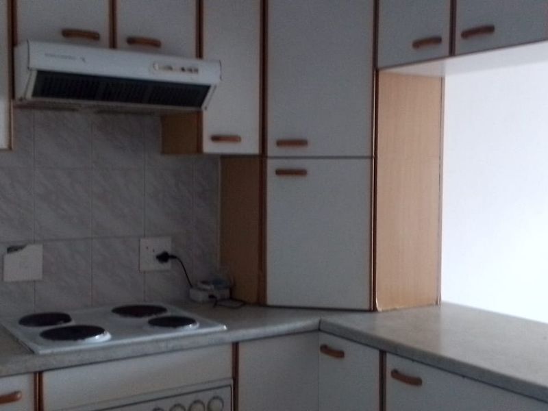 A dated kitchen featuring white cabinetry with wood trim, an electric hob, extractor fan, and tiled backsplash, requiring cosmetic updates.