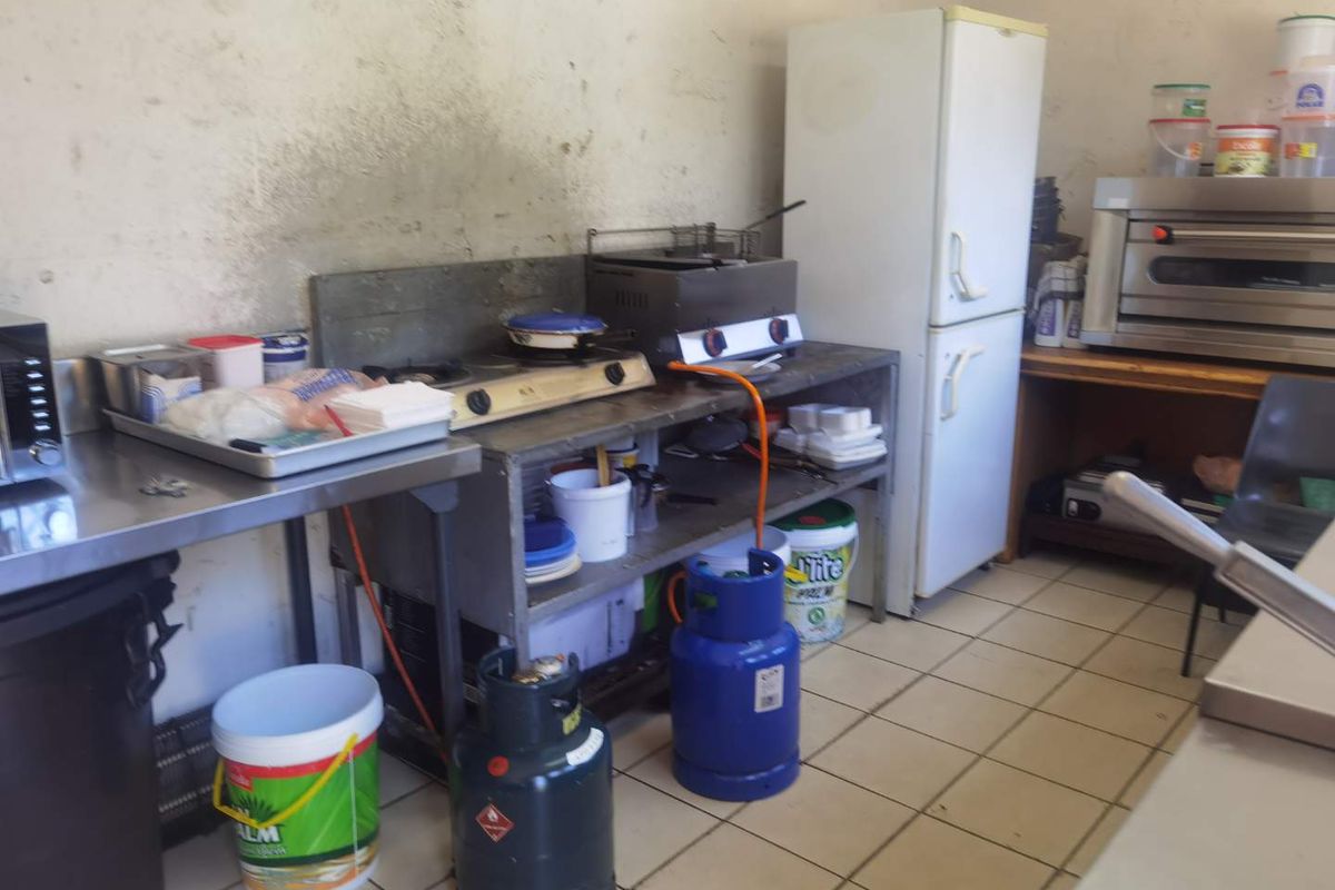 A functional commercial-style kitchen area featuring stainless steel prep surfaces, gas cooking hobs, and tiled flooring.
