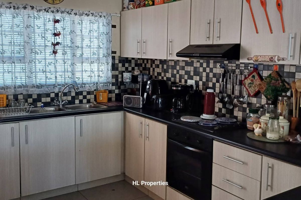 A functional kitchen featuring light-toned laminate cabinetry, black countertops, a built-in oven with extractor fan, and a classic checkerboard tiled backsplash.