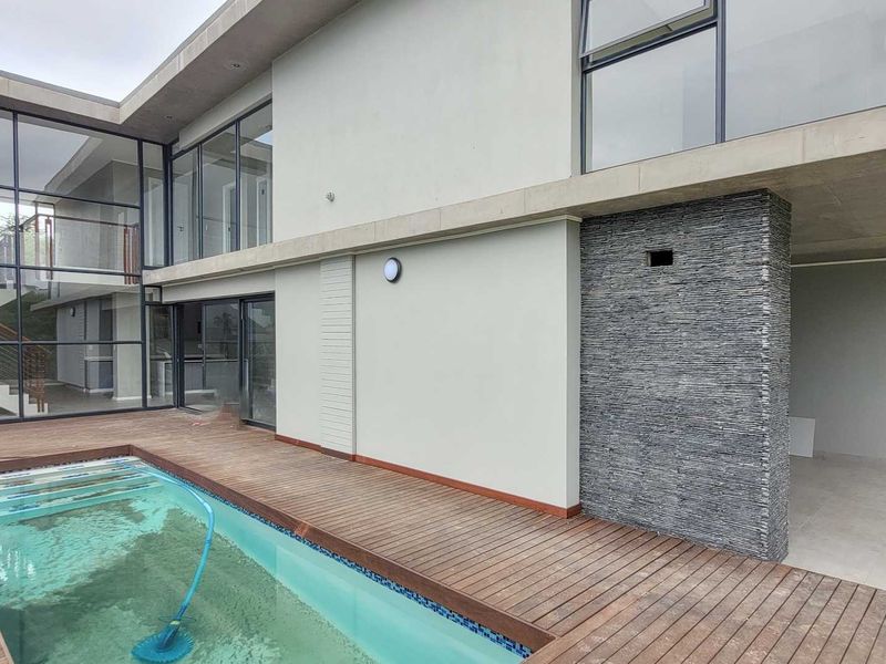 Modern outdoor pool area featuring timber decking, a stone-clad feature wall, and large glass sliding doors leading into the residence.