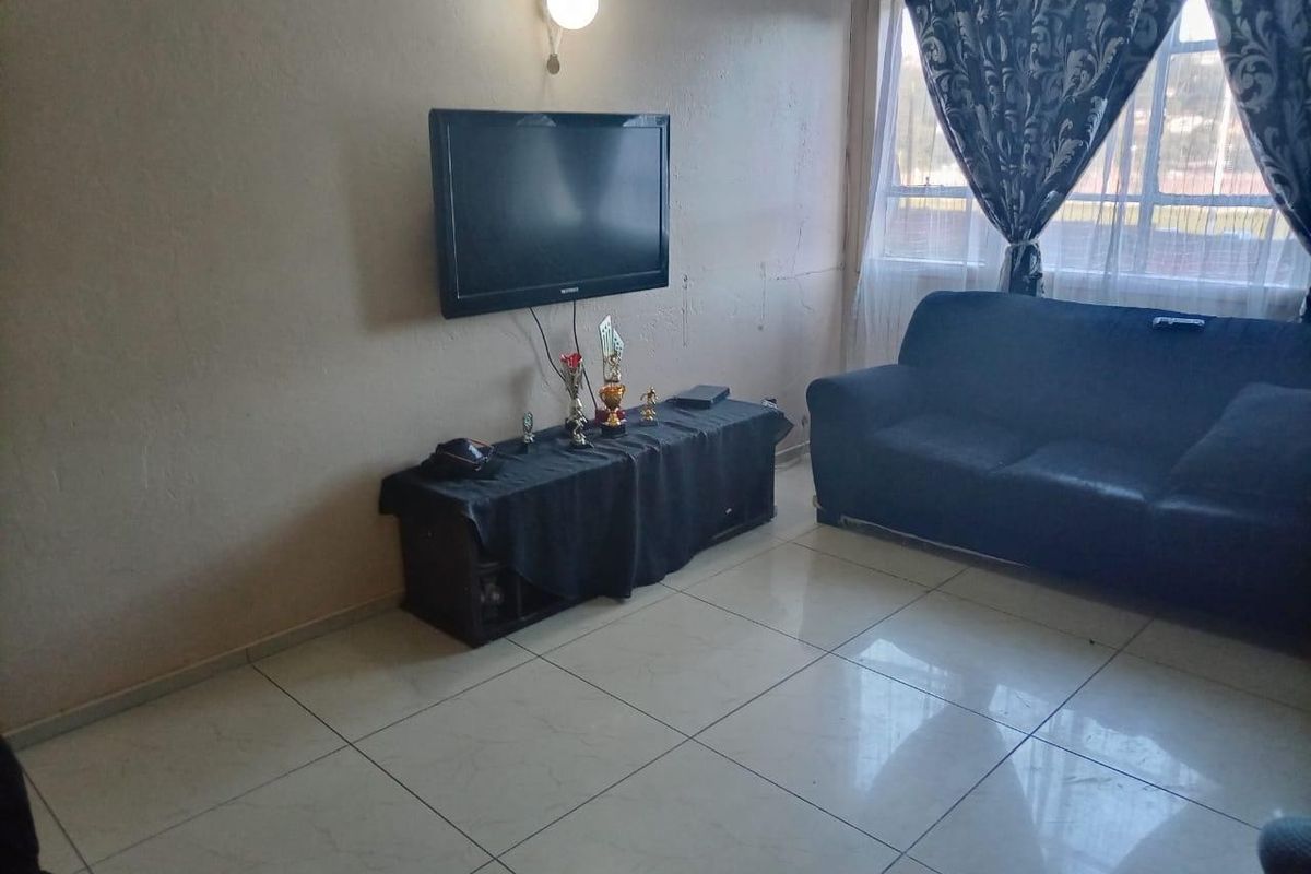 A living room featuring tiled flooring and a wall-mounted light fixture, showing signs of wear on the wall surfaces.