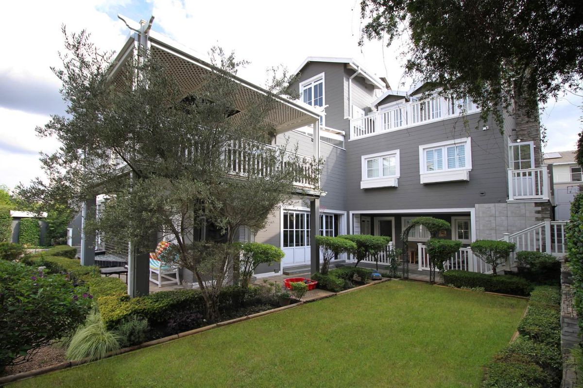 A well-maintained multi-level rear exterior featuring a landscaped garden, a covered deck with a pergola, and upper-level balconies.