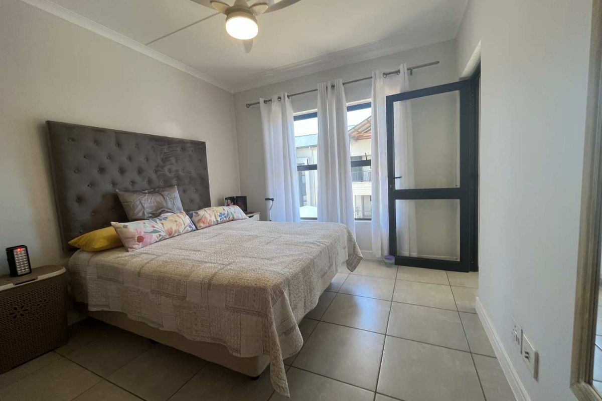 A well-lit bedroom featuring tiled flooring, a ceiling fan, and a glass-panelled door providing access to the exterior.