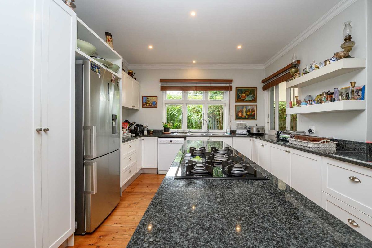 A well-appointed kitchen featuring a large central island with a built-in gas hob, granite countertops, white cabinetry, and timber flooring.