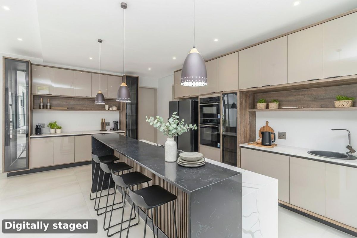 Modern kitchen featuring sleek cabinetry, a large stone-topped island with breakfast bar seating, built-in ovens, and integrated appliances.