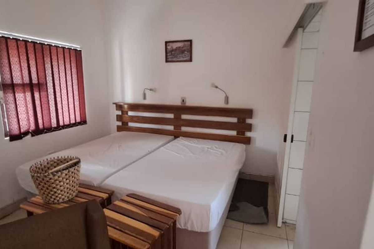 A functional bedroom featuring tiled flooring, a built-in wooden headboard, and wall-mounted reading lights.