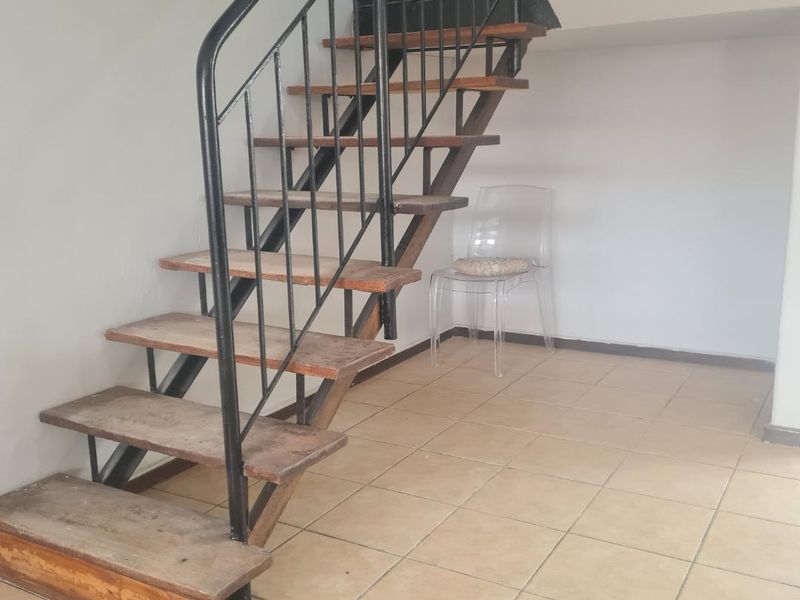 A hallway area featuring an open-tread staircase with a metal balustrade and tiled flooring, showing signs of wear and tear.