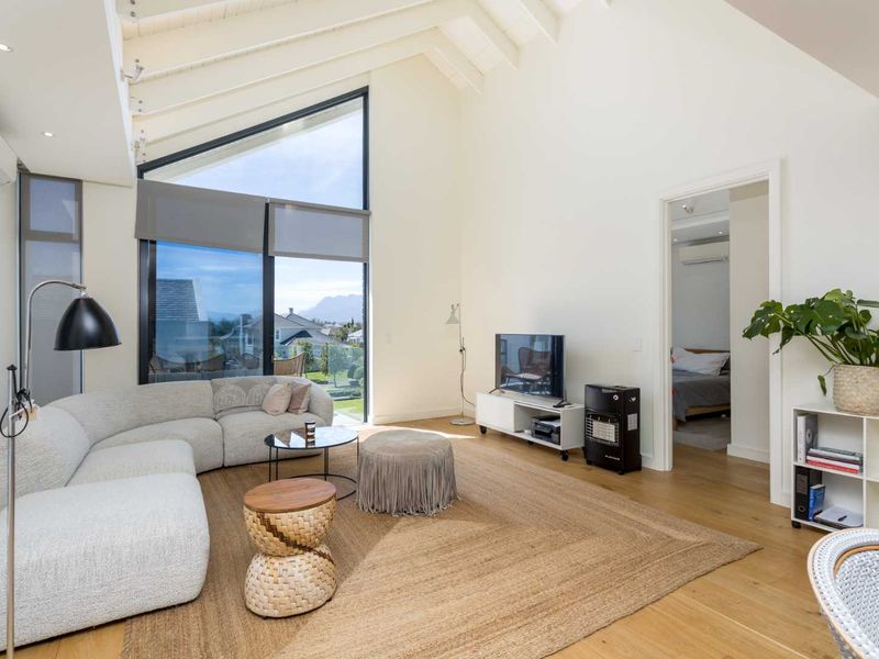 Spacious living room featuring high vaulted ceilings with exposed rafters, timber flooring, and a large floor-to-ceiling window offering natural light and scenic views.