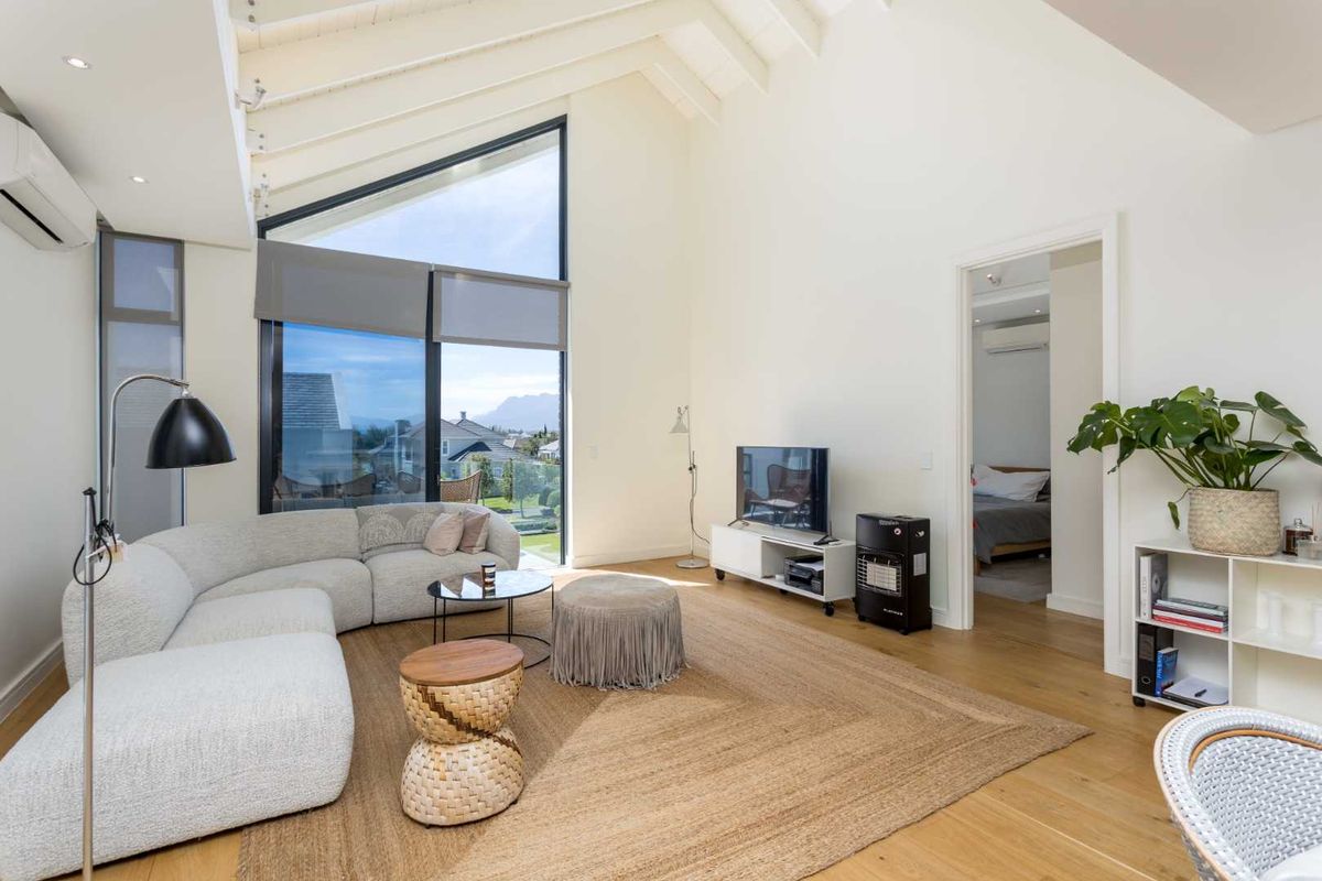 Spacious living room featuring high vaulted ceilings with exposed rafters, timber flooring, and a large floor-to-ceiling window offering natural light and scenic views.
