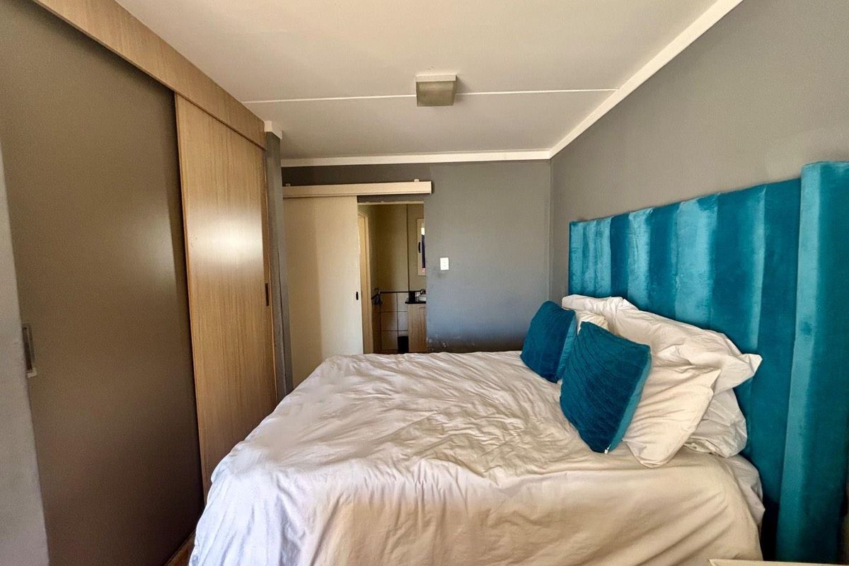 A bedroom featuring a built-in sliding door wardrobe and an adjoining ensuite bathroom, with neutral grey walls and a functional layout.