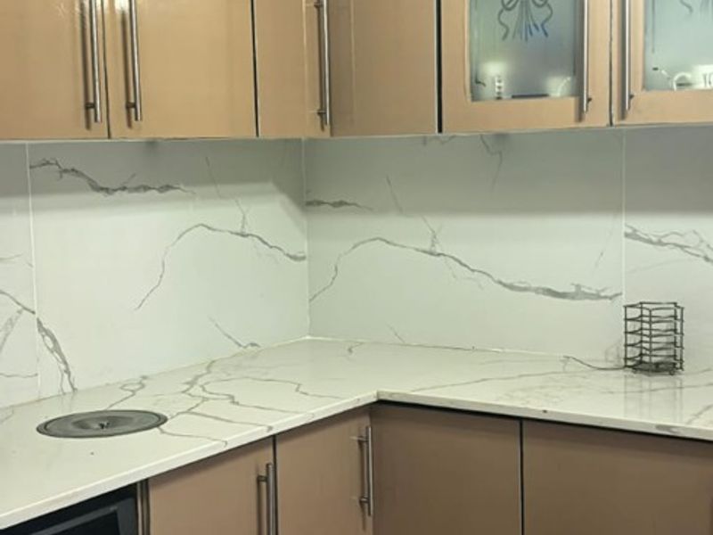 A functional kitchen area featuring modern marble-effect countertops and backsplash, complemented by neutral-toned cabinetry and ceramic floor tiling.