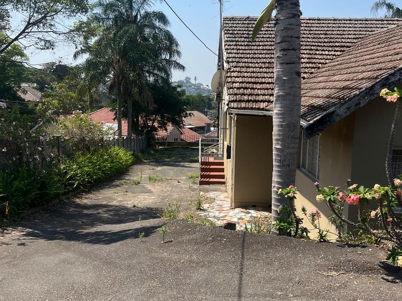 Rear exterior view of the property featuring a concrete driveway, tiled roof, and paved walkway leading to the back entrance.