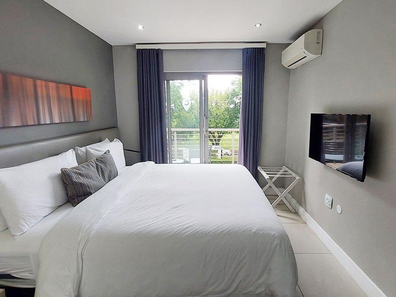 A well-maintained bedroom featuring tiled flooring, a split-system air conditioner, and a sliding glass door providing access to a balcony.