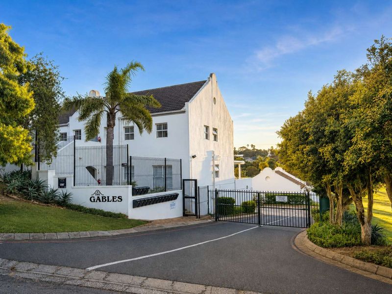 The entrance to The Gables townhouse complex, featuring a secure gated driveway, white facade architecture, and landscaped surroundings.