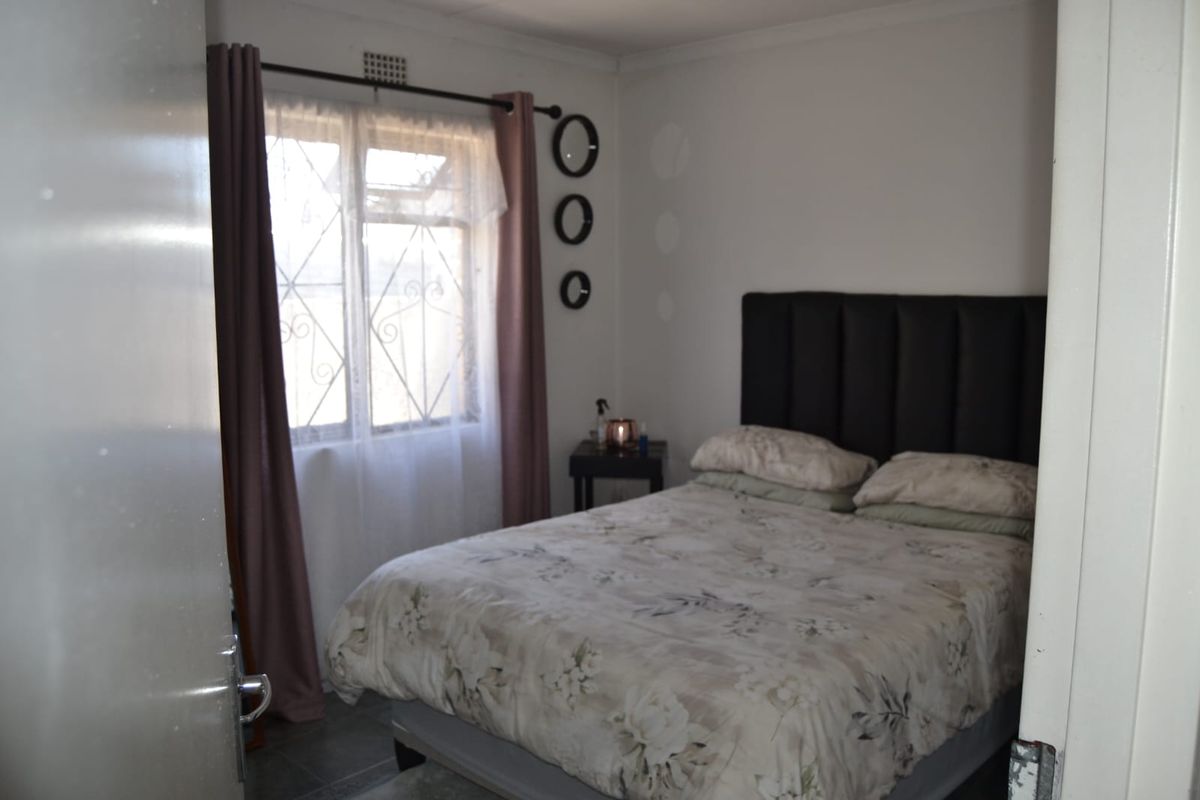 A functional bedroom featuring tiled flooring, security burglar bars on the window, and decorative cornice detailing.