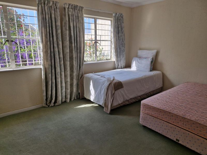 A bedroom featuring carpeted flooring and windows fitted with security bars, offering natural light and a view of the garden.