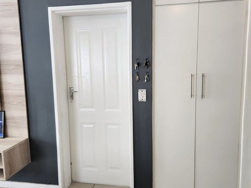 A clean hallway featuring neutral tiled flooring, a white interior door, and a tall built-in storage cupboard with modern handles.