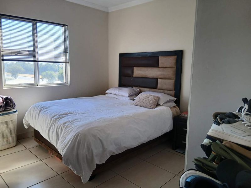 A functional bedroom featuring tiled flooring, neutral wall tones, and a window fitted with venetian blinds, providing natural light.
