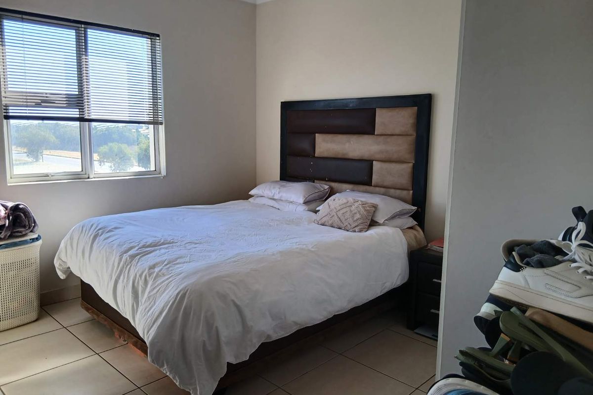 A functional bedroom featuring tiled flooring, neutral wall tones, and a window fitted with venetian blinds, providing natural light.