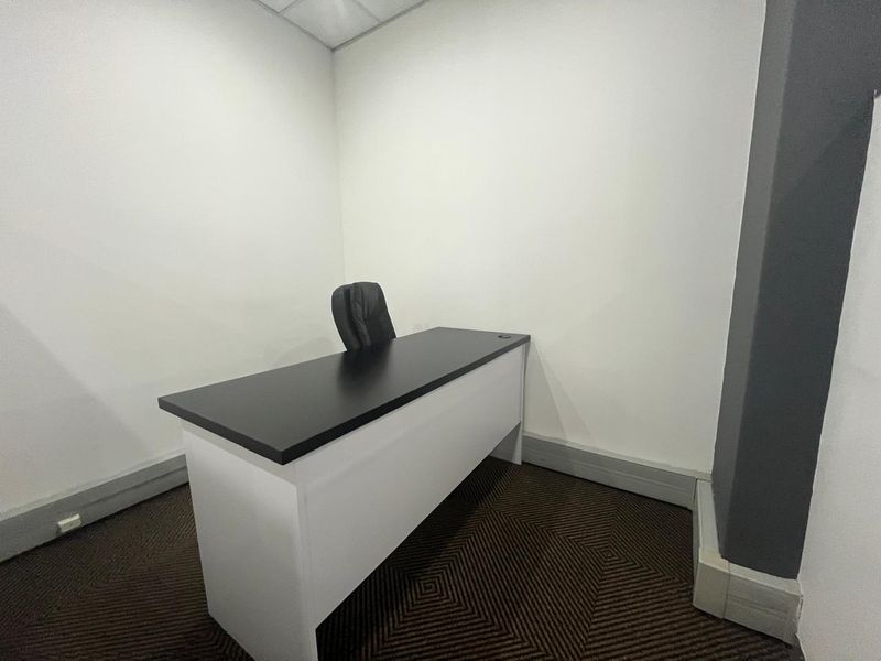 A compact, functional office space featuring neutral walls, carpeted flooring, and a suspended ceiling, suitable for a private workspace or small meeting room.