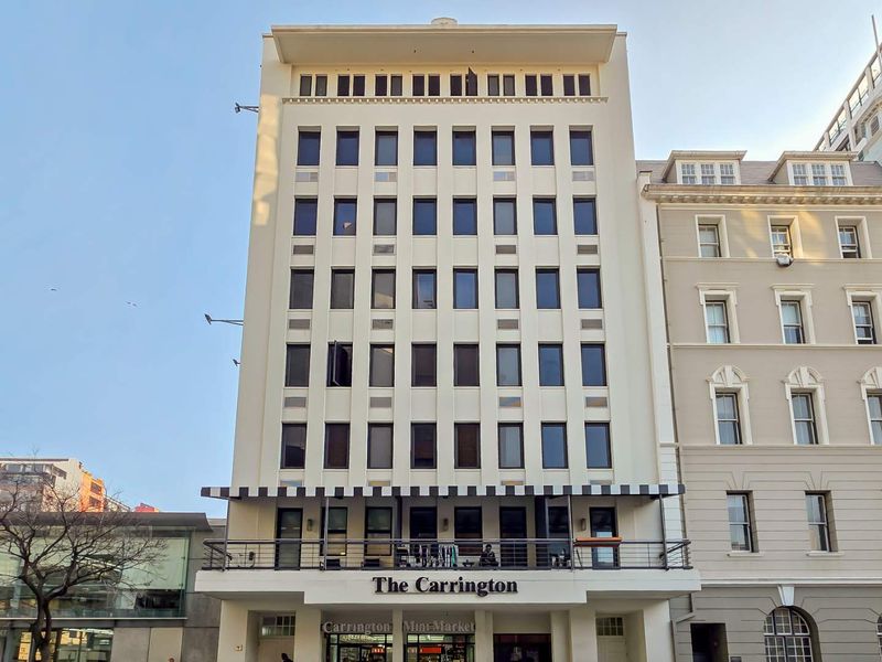 Front elevation of The Carrington apartment building, featuring a multi-story facade with a balcony, striped awning, and ground-floor commercial space.